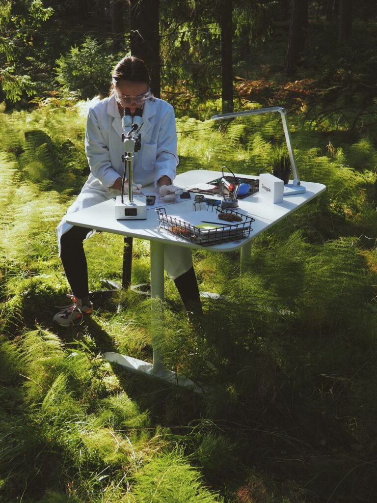 Scientist in lab coat conducting research with microscope in forest environment.
