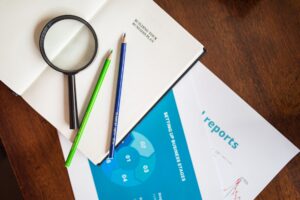 A top view of a magnifying glass, colored pencils, and business reports on a wooden table.
