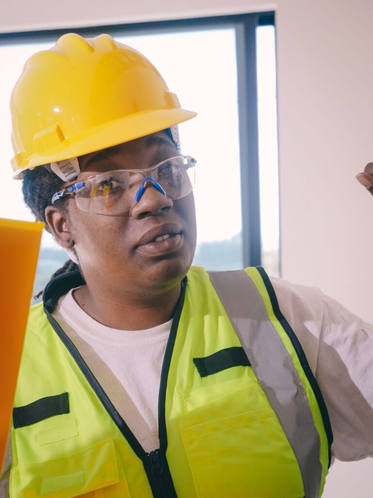 Professional black female engineer wearing safety gear, hardhat, and reflective vest at a construction site.
